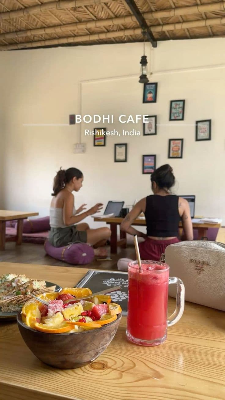 Inside Bodhi Cafe in Rishikesh, guests working at low wooden tables on floor cushions under a thatched roof