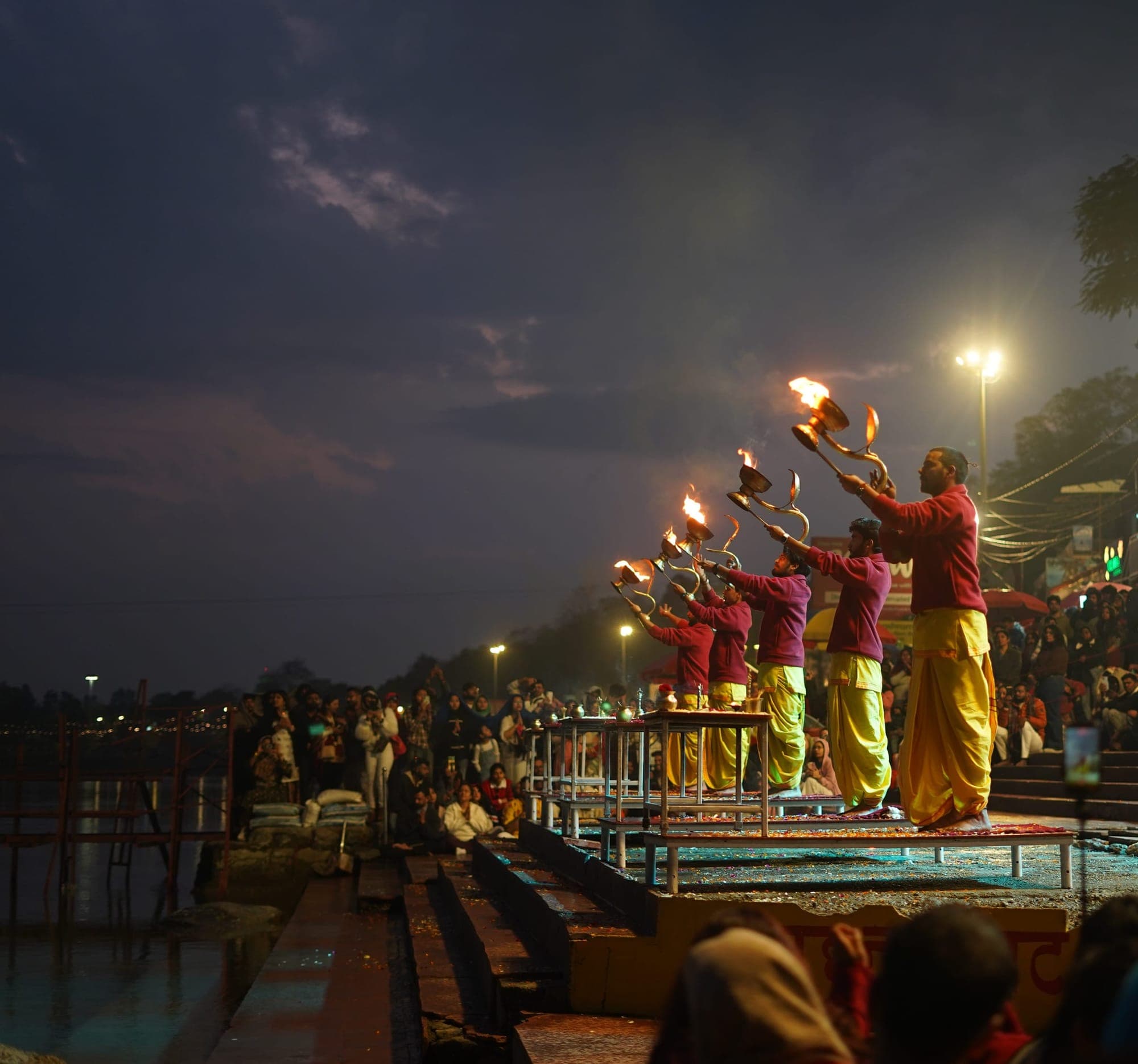 Priests raising flaming lamps at the evening Ganga Aarti in Rishikesh, dusk light over the river