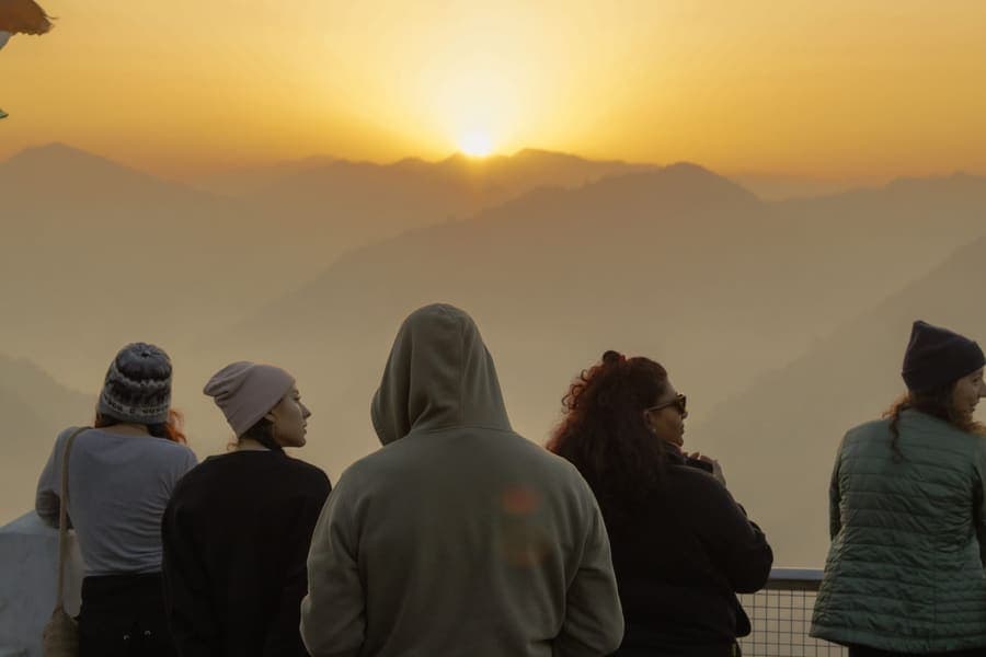 A group of travellers at a railed viewpoint watching sunrise over the Himalayan foothills