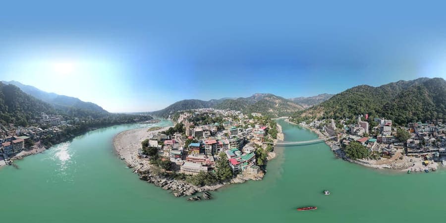 Aerial panorama of Rishikesh with the turquoise Ganga curving past riverside buildings and a suspension footbridge