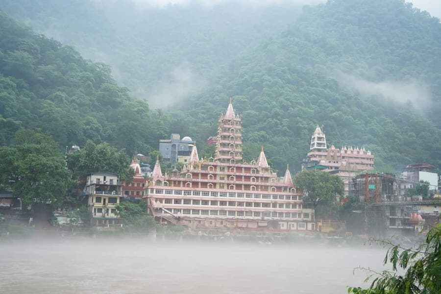 The pink tiered Tera Manzil temple on the Ganga riverbank at Laxman Jhula, Rishikesh, seen through monsoon mist