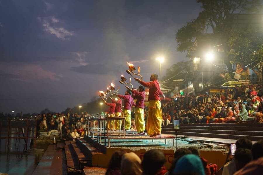 Row of priests lifting flaming brass lamps during the evening Ganga Aarti ceremony on the ghats of Rishikesh at twilight
