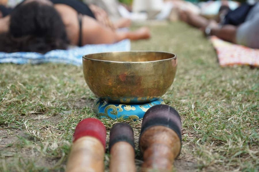 Brass singing bowl on a blue cushion on grass with wooden mallets during an outdoor sound healing session