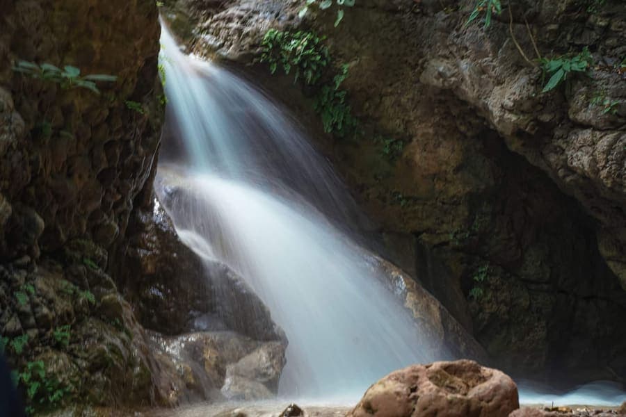 Waterfall cascading over rock into a shallow pool in a forested gorge near Rishikesh