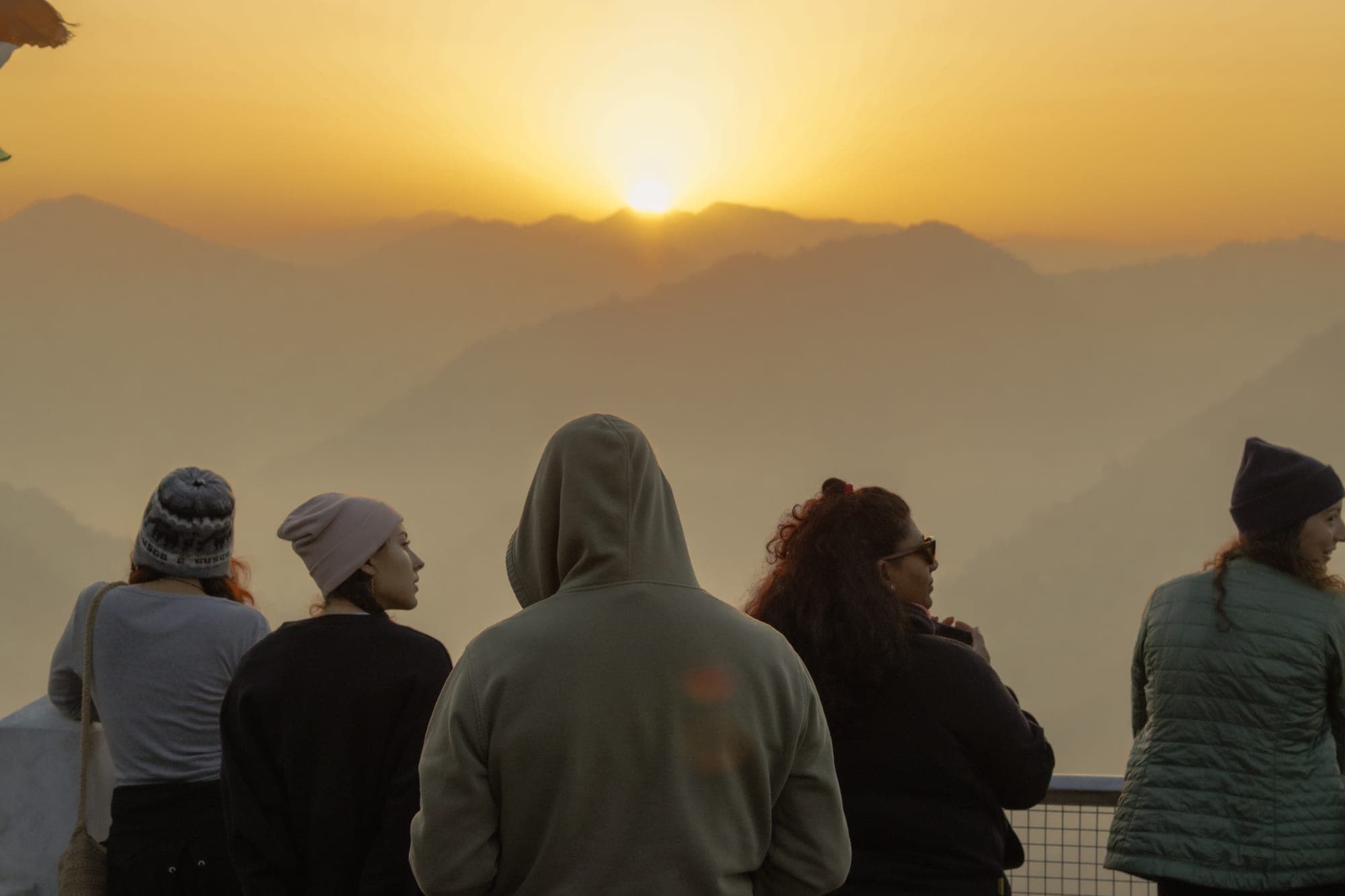 A group of travellers at a railed viewpoint watching sunrise over the Himalayan foothills