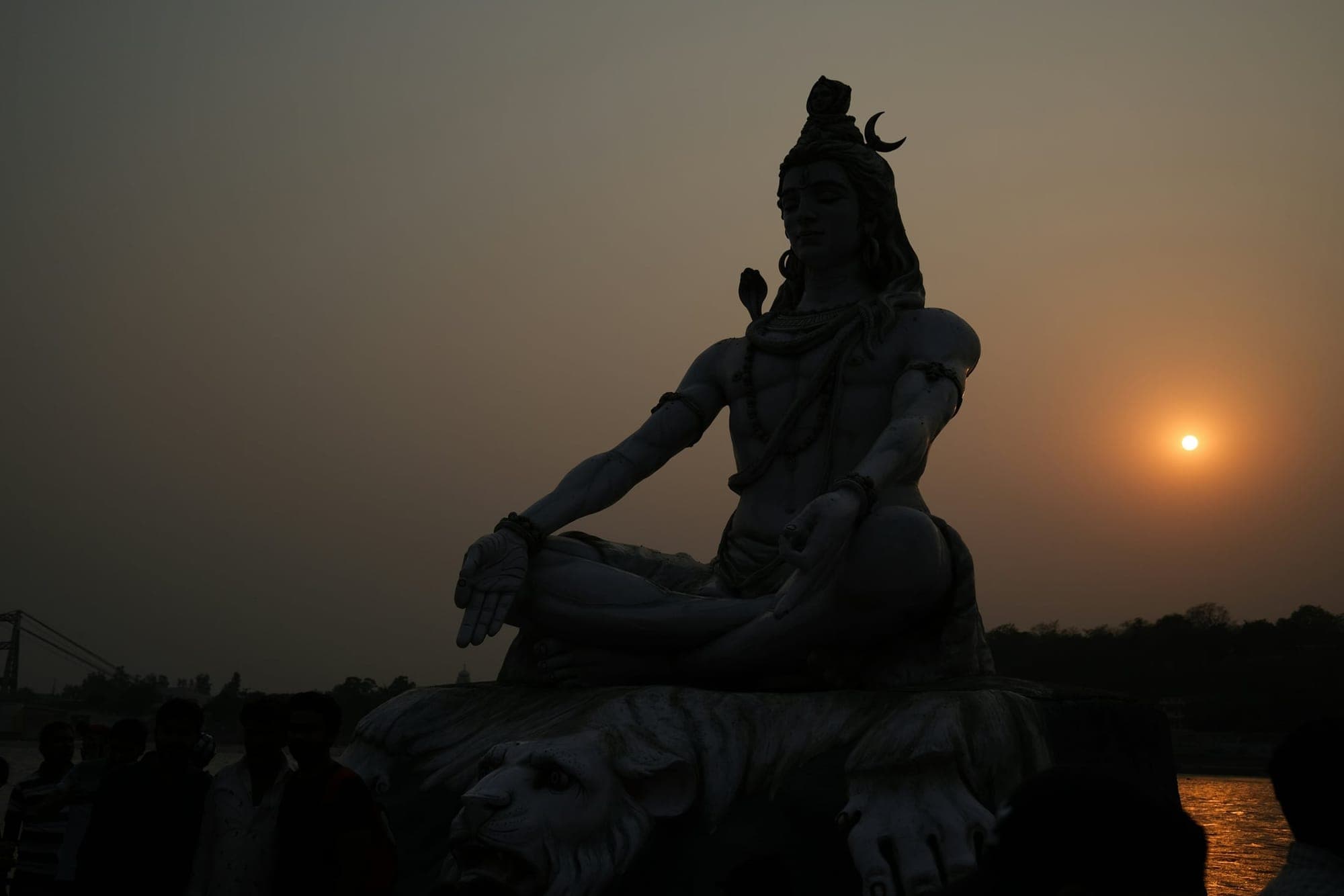 The large seated Shiva statue on the bank of the Ganga at Rishikesh, lit at dusk with the river and the hills behind