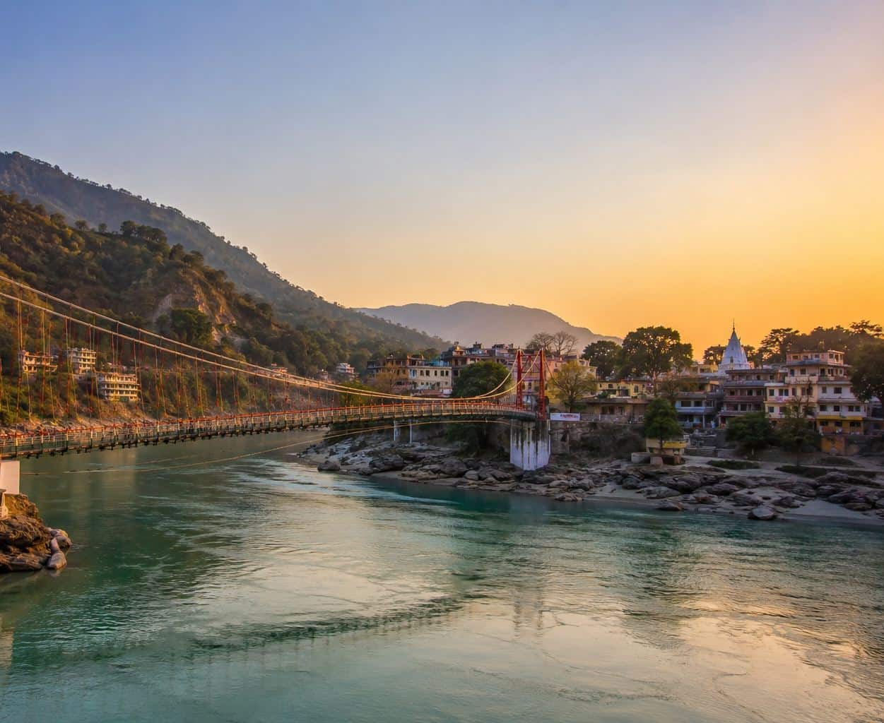 The Ganga at dusk in Rishikesh, a suspension bridge and the temple town along the bank