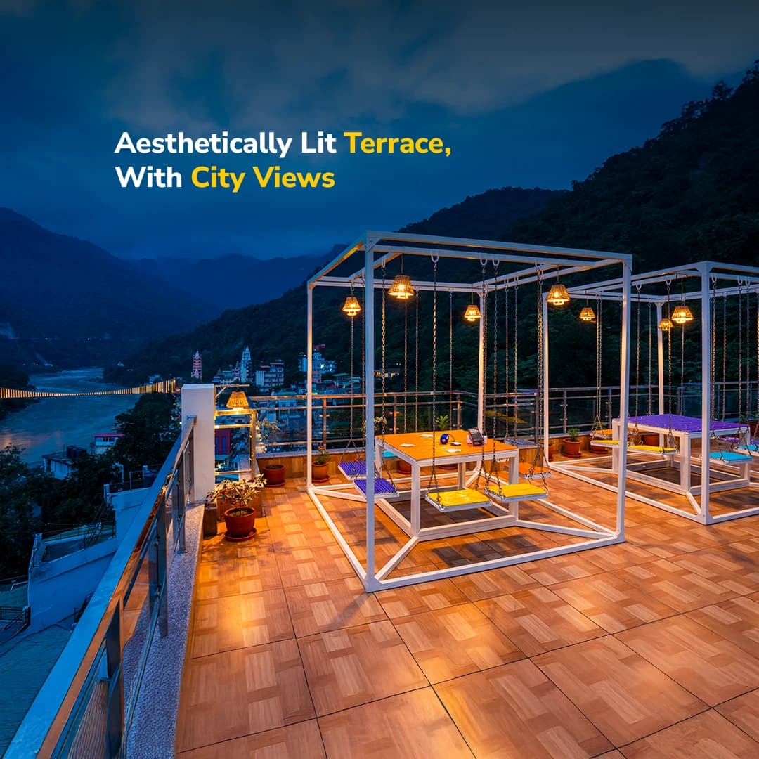 Rooftop terrace lit up in the evening at goSTOPS Rishikesh, Lakshman Jhula, with the Lakshman Jhula bridge visible below
