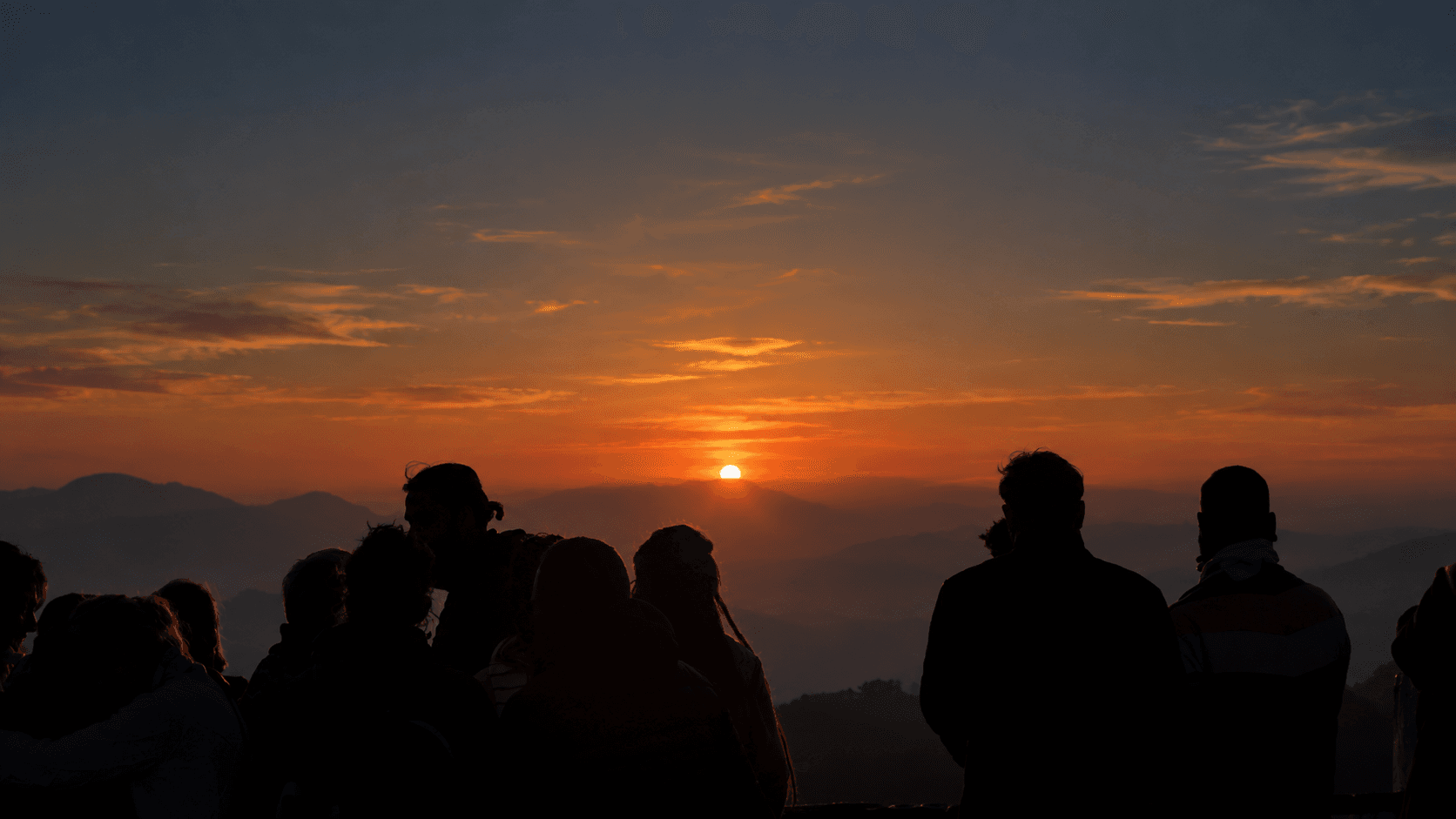 Silhouetted travellers watching a vivid orange and pink sunrise over the Himalayan foothills near Rishikesh
