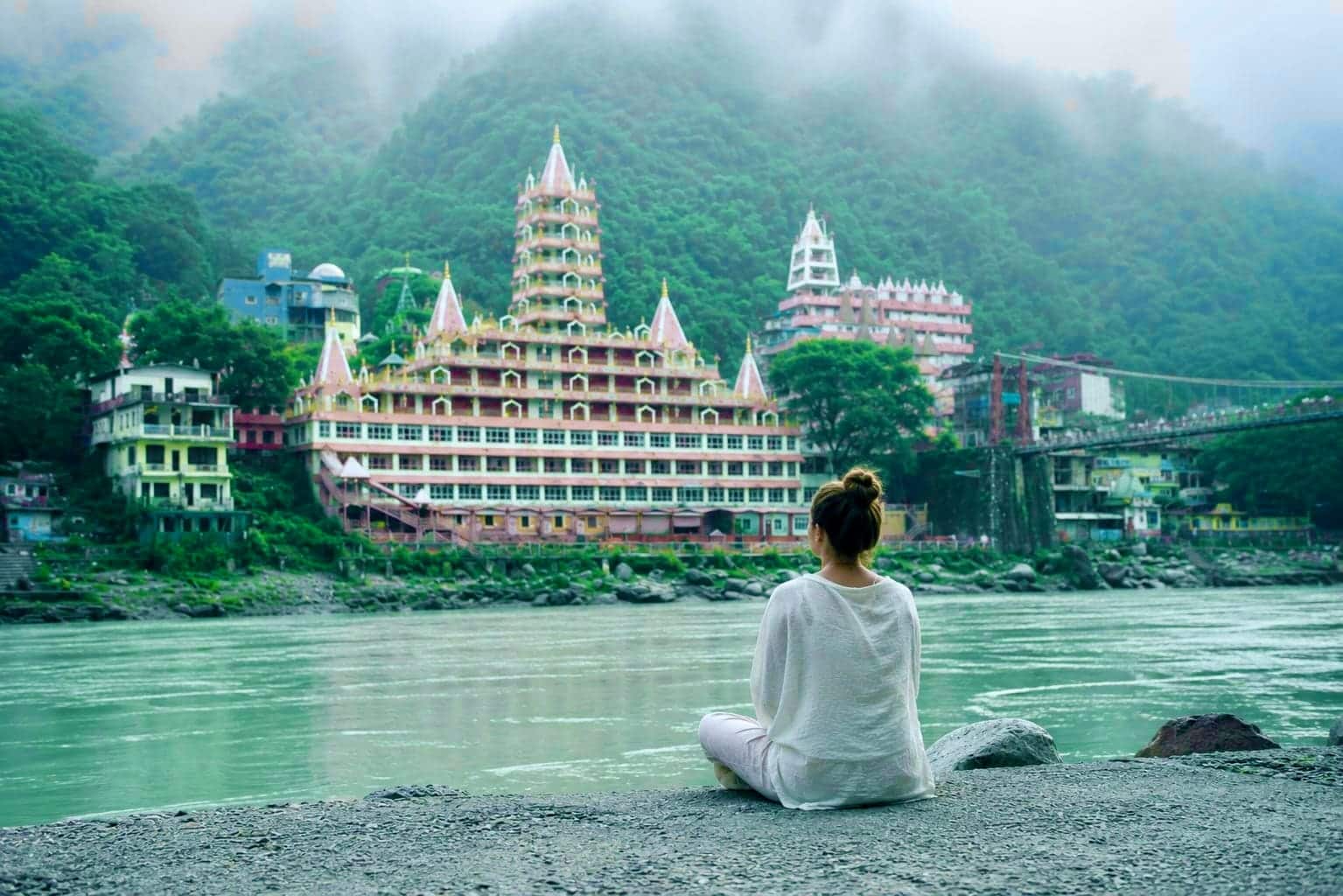 A woman meditating cross-legged on a ghat beside the Ganga in Rishikesh at first light