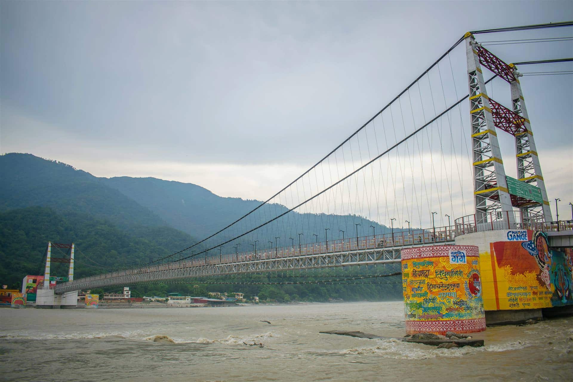The Janki Setu footbridge over the Ganga in Rishikesh, with painted piers and forested hills behind