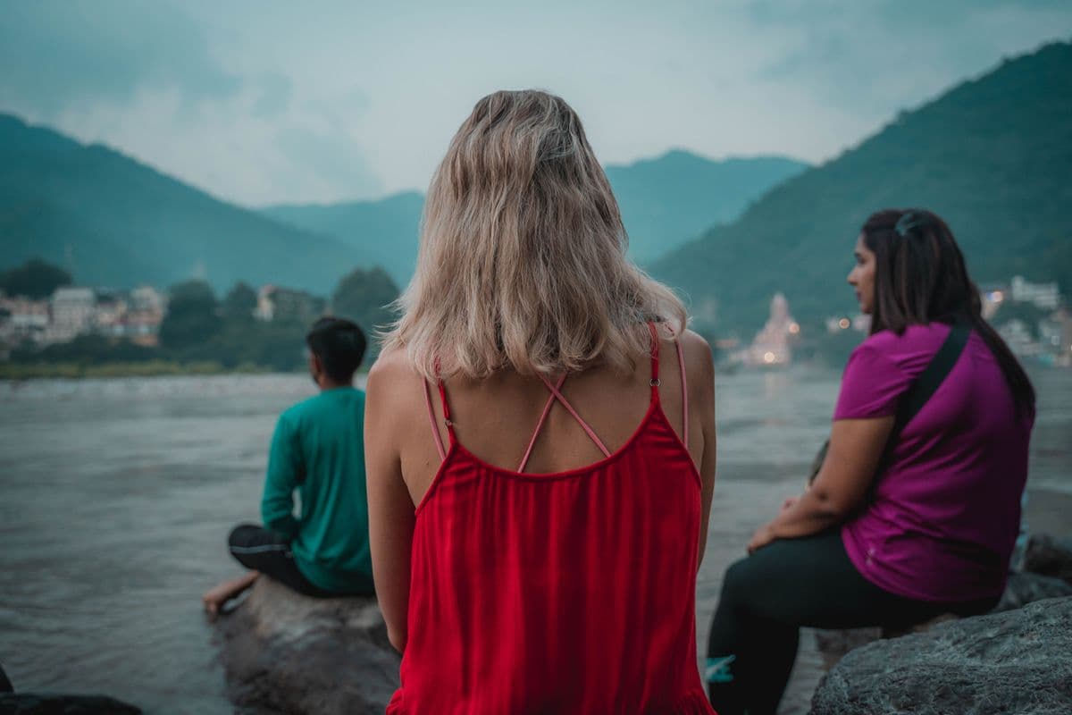 Three travellers sitting quietly on the rocks beside the Ganga at dusk in Rishikesh